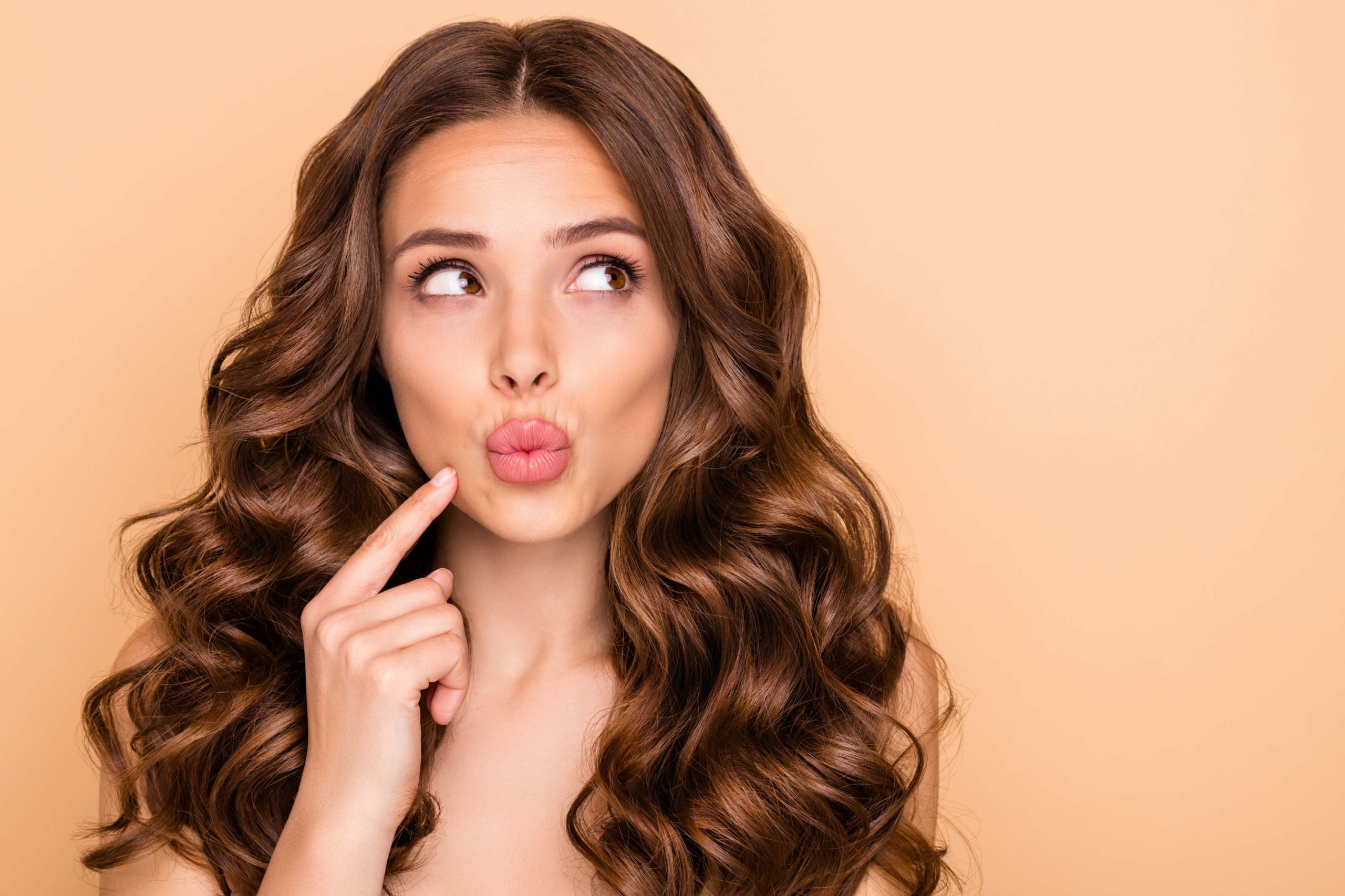 Pretty girl with cute pose holding finger on near lips | Lip Fillers at Beauty Boost Med Spa in Newport Beach, CA